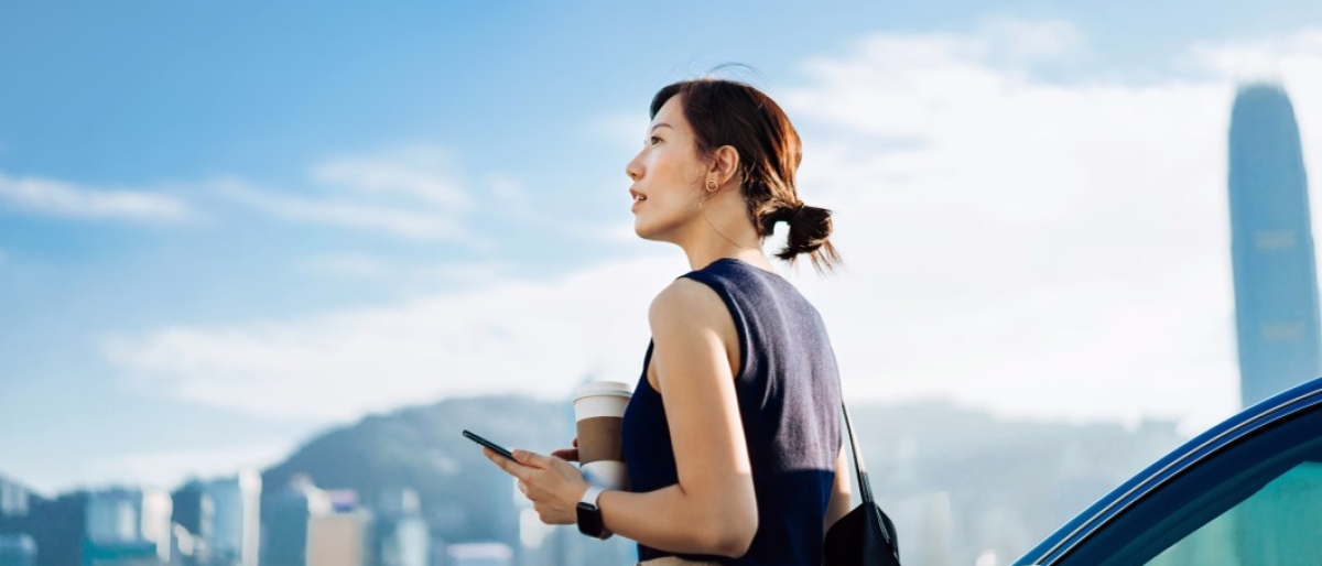 Person holding a phone and coffee with city skyline in the background.