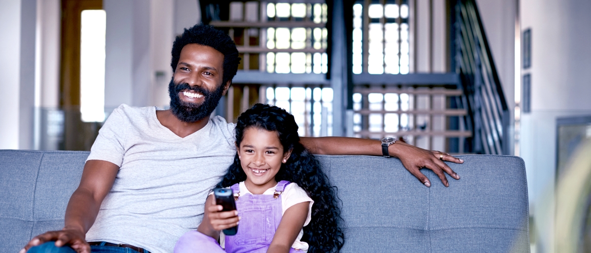 Image of a father and daughter sitting on couch watching television