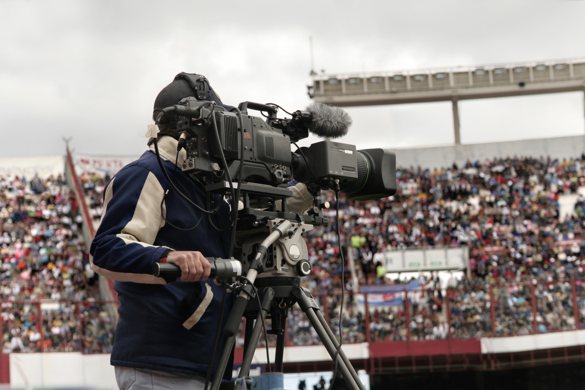 A cameraman films a sports event in a packed stadium.