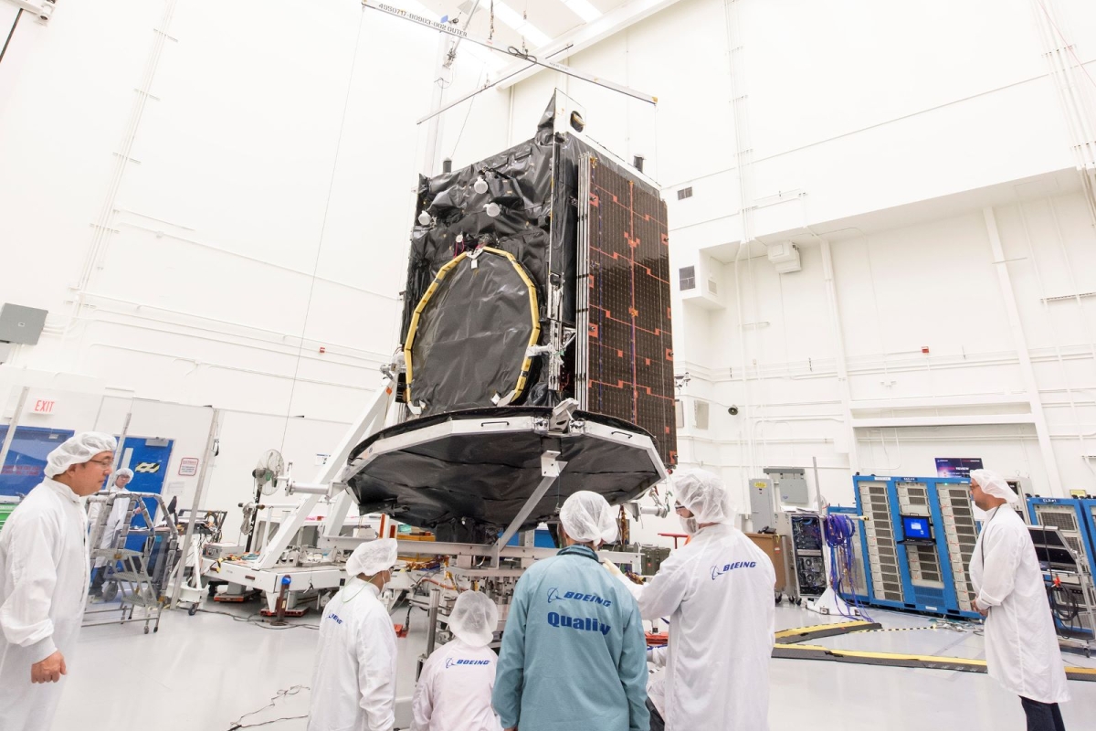 Team of engineers in front of a satellite component in a white room