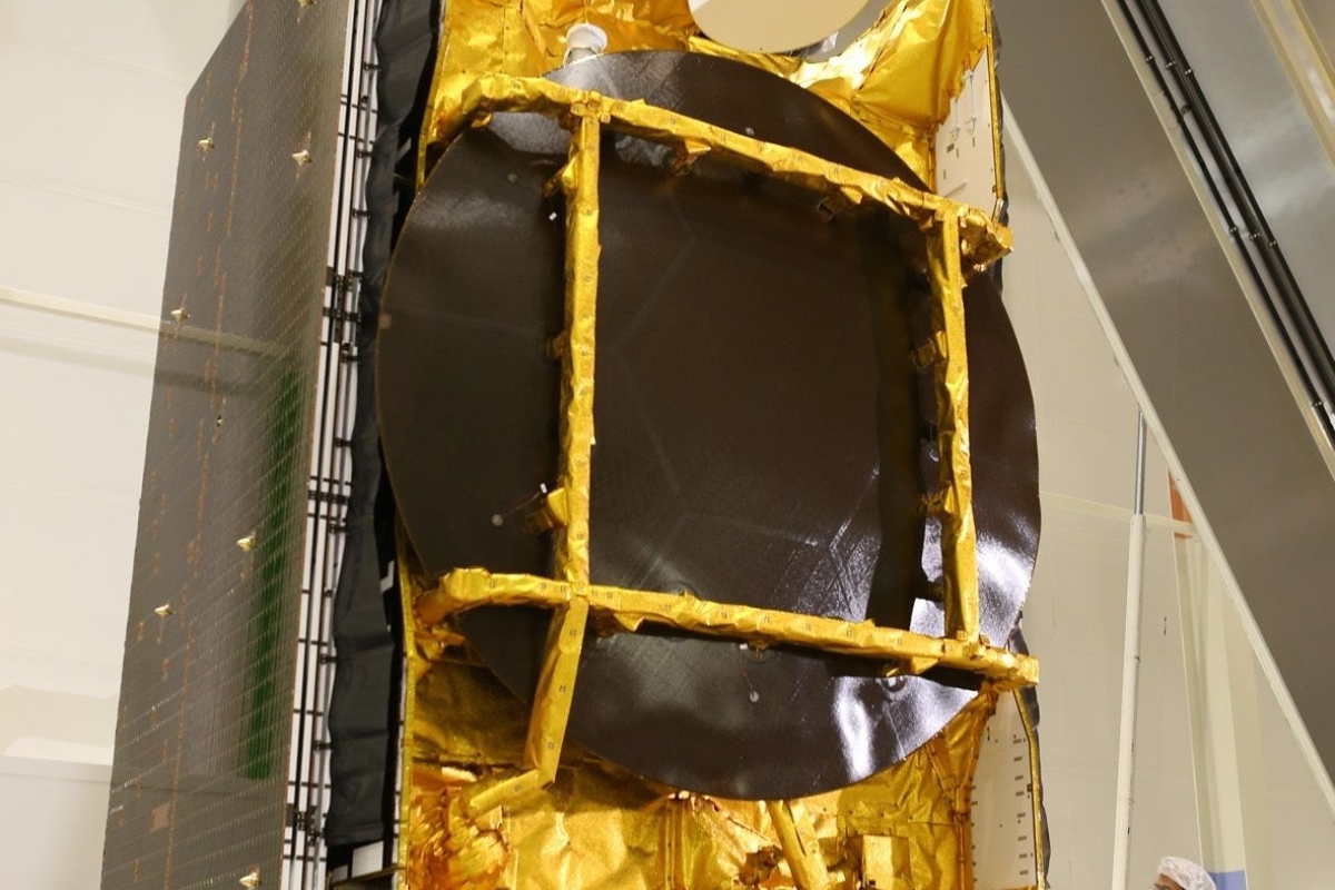 Technical operator next to satellite bus covered with golden thermal blanket in a clean room
