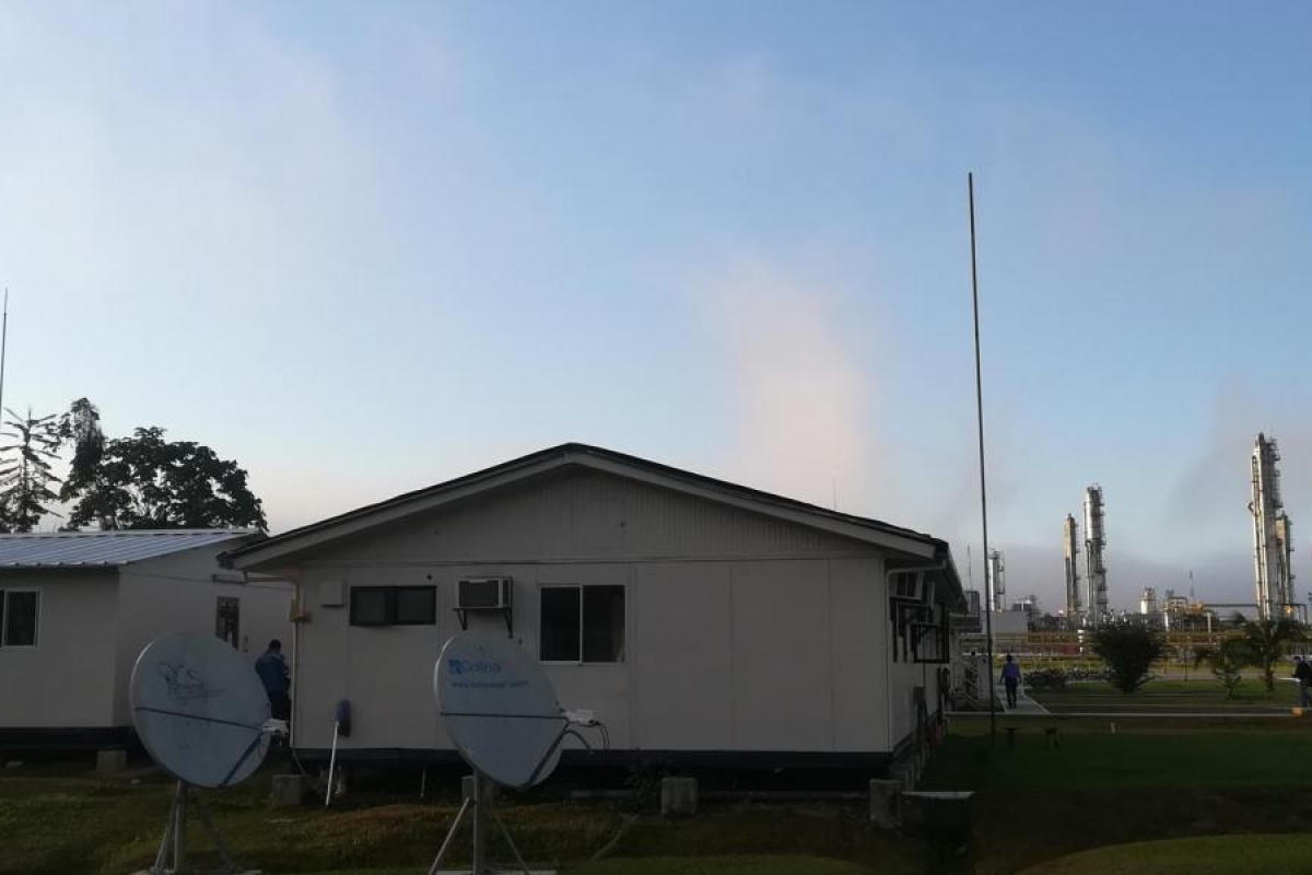 Image of satellite dishes outside small buildings near an industrial facility.