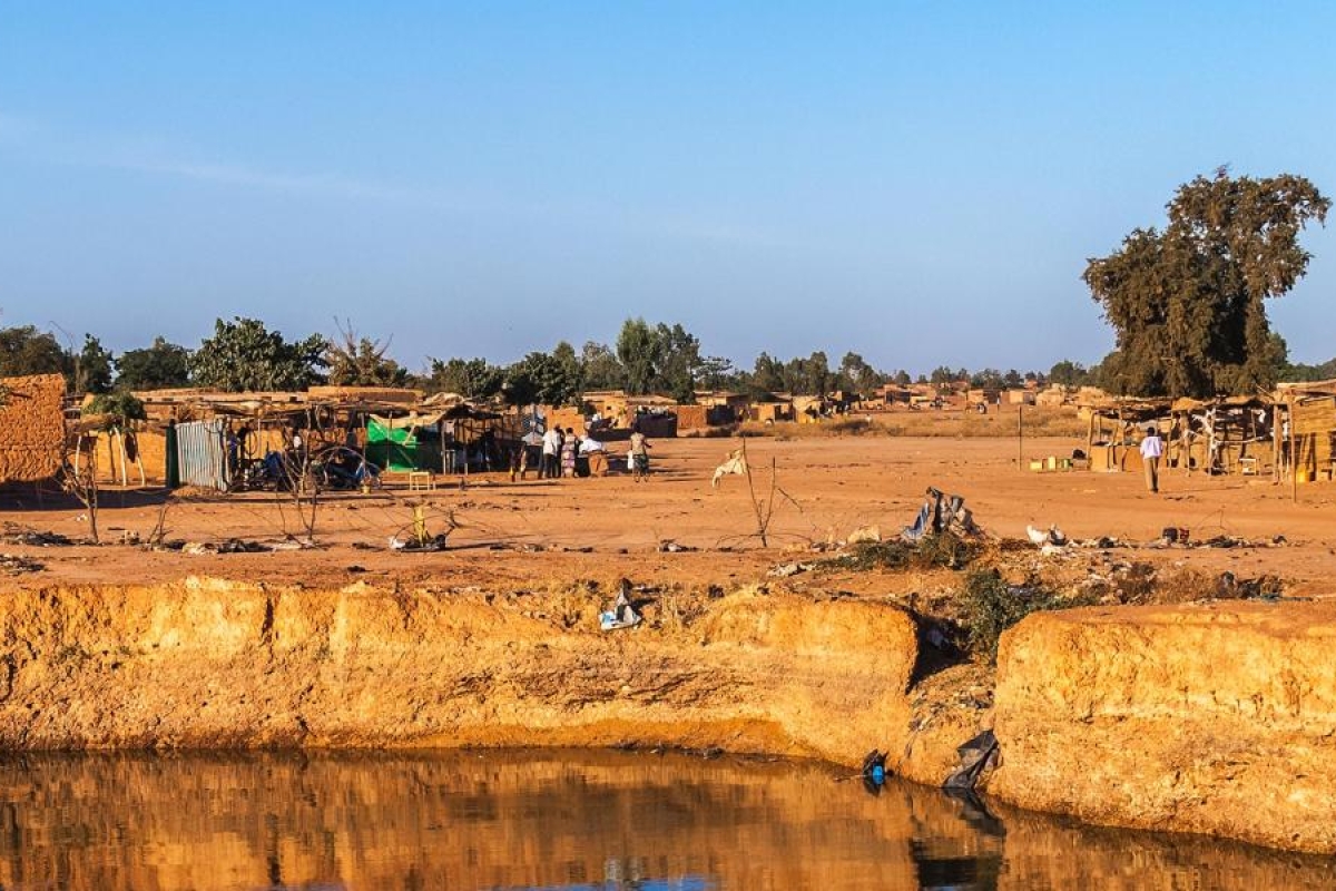 Image of a rural desert village with small clay structures and a water channel in the foreground
