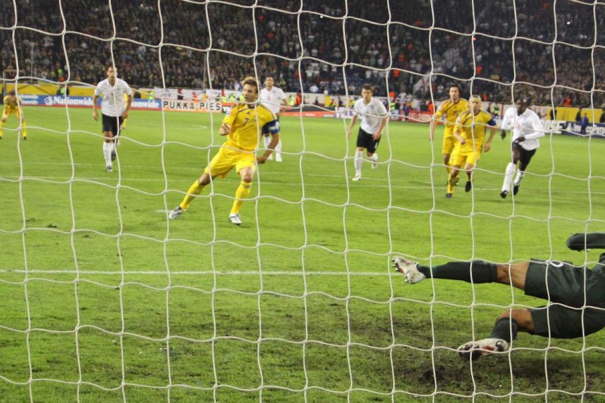 Image of goalkeeper diving as the ball heads toward the net during a football match.
