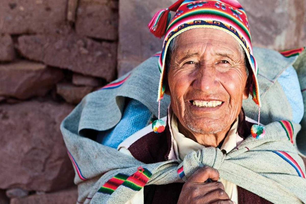 Image of a person in traditional woven clothing standing against a stone wall.