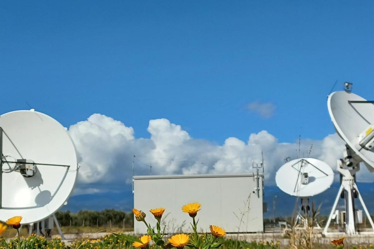 Image of satellite dishes in a field with yellow flowers under a bright blue sky.