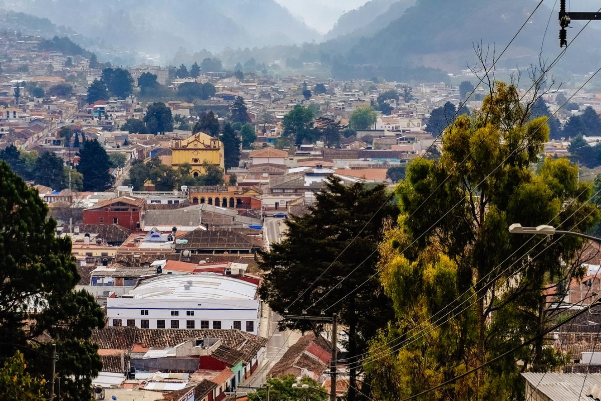 Landscape image of hillside view overlooking a dense town surrounded by mountains and trees.