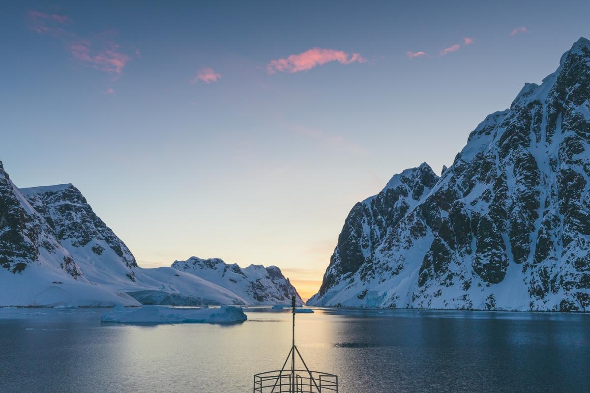 Image of a Ship cruising through icy fjord at sunset between snow-covered mountains