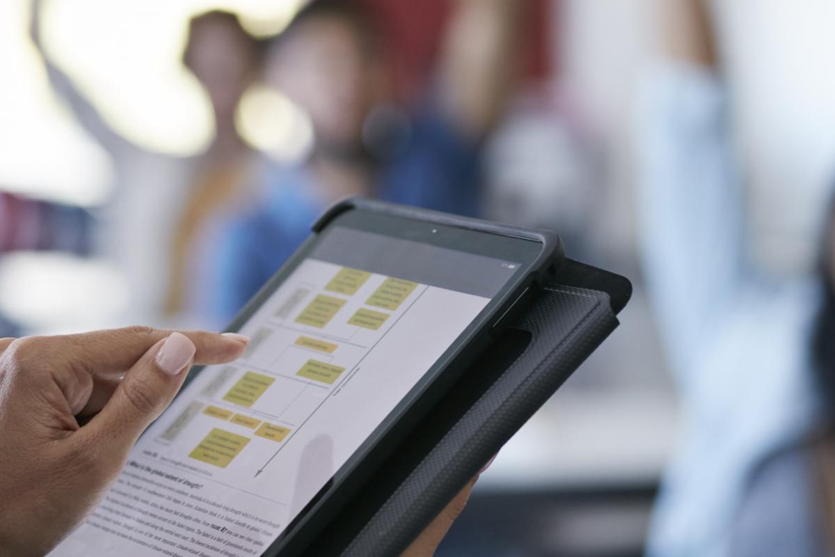 Image of a person holding a tablet displaying a flowchart in a classroom setting.