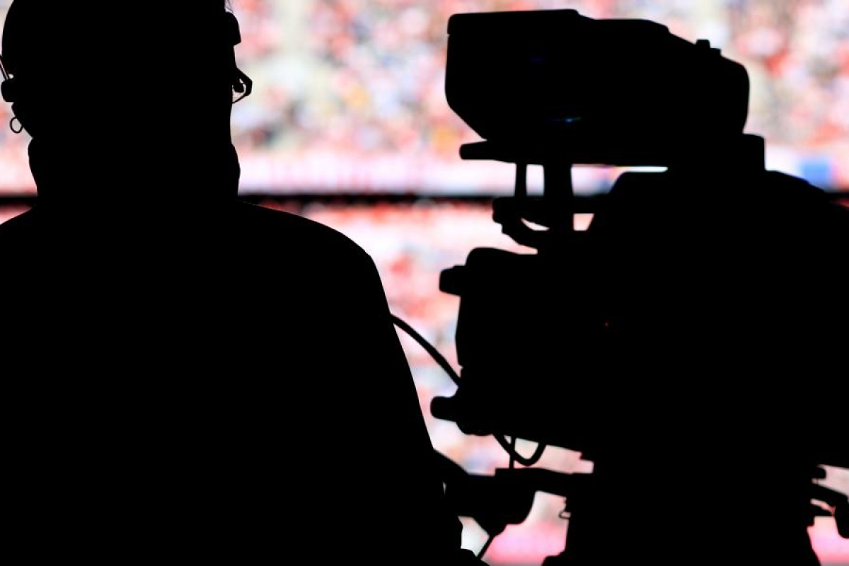 Image of a camera operator's silhouette filming with a broadcast camera.