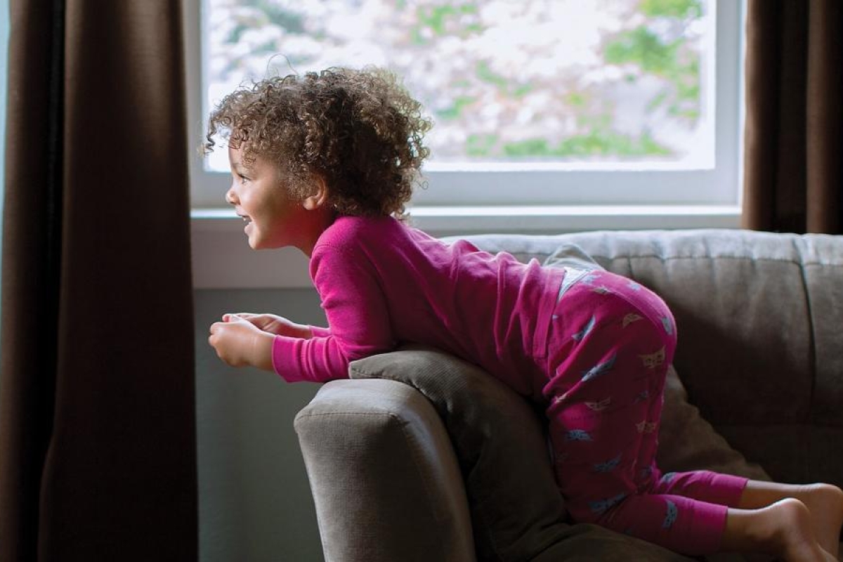 Image of a child in pajamas kneeling on a couch watching TV.