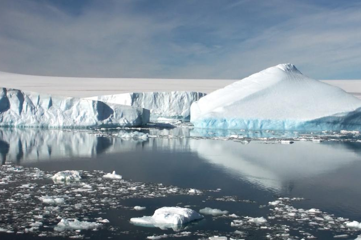 Landscape image of a large iceberg reflecting on calm Arctic water.
