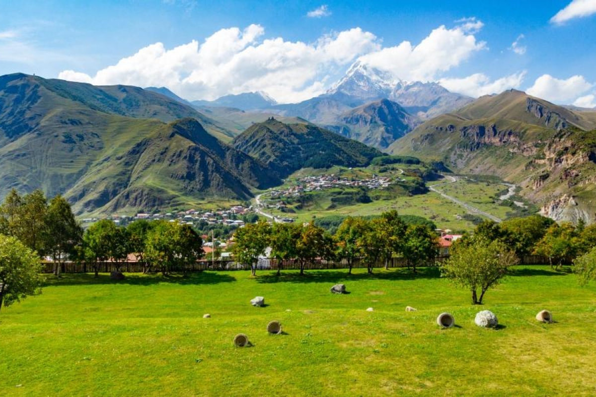 Image of a landscape with green valley with scattered trees and distant mountain peaks.