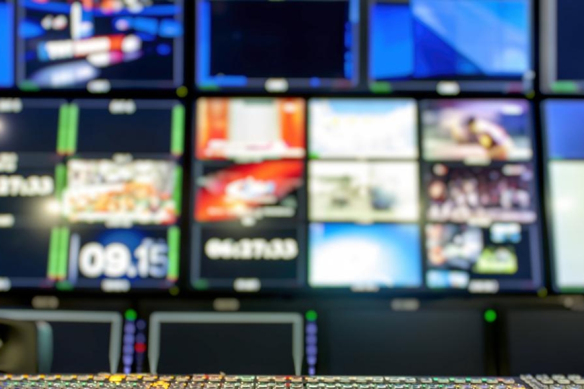 Broadcast control room with a switcher panel and multiple screens.