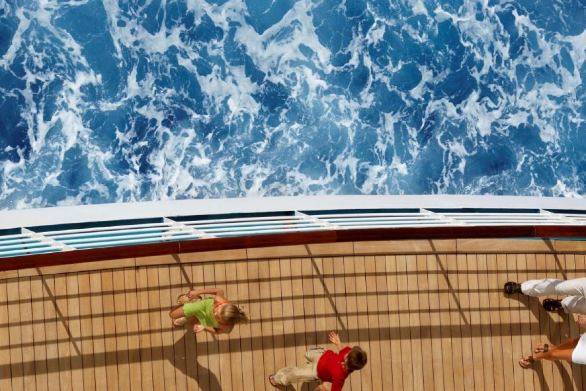 Top‑view image of a cruise ship deck beside deep blue ocean water.