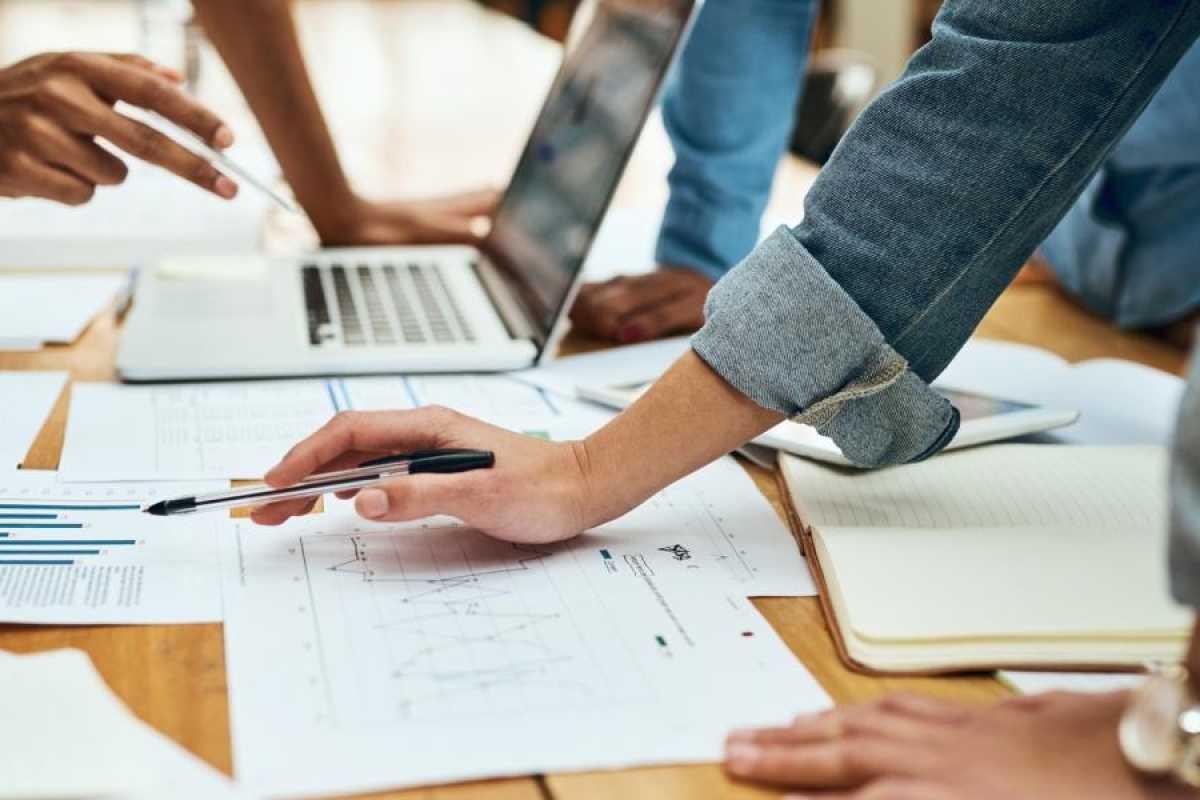 Closeup image of employees working at a table with laptops, papers and pens