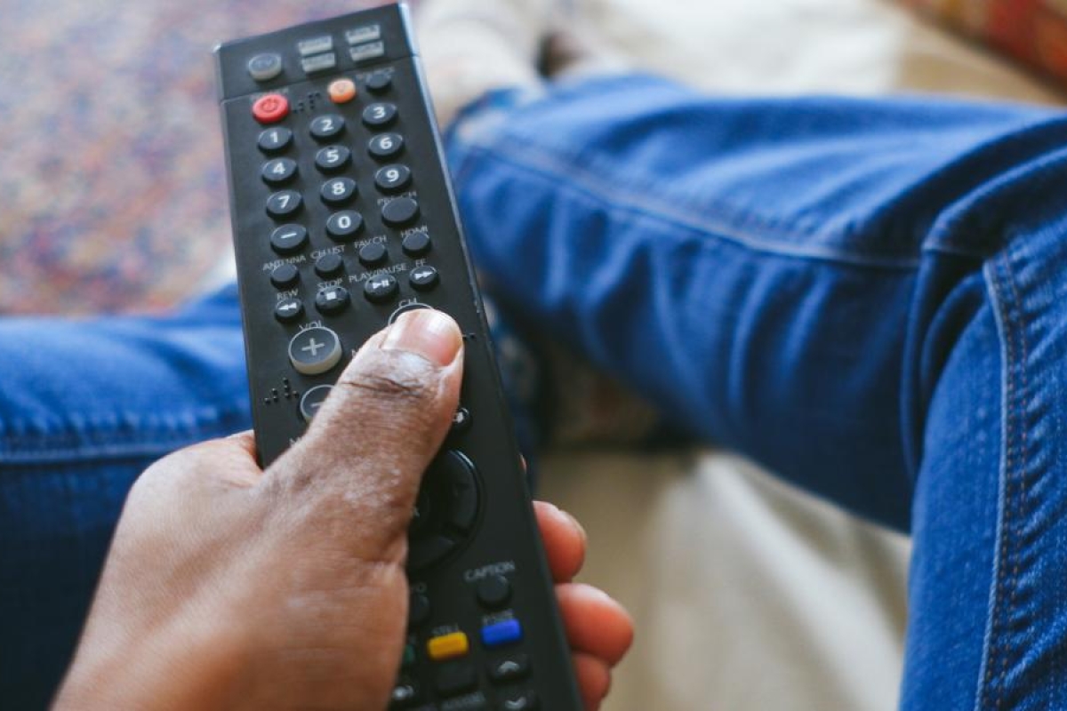 Close‑up image of a hand holding a TV remote while seated.