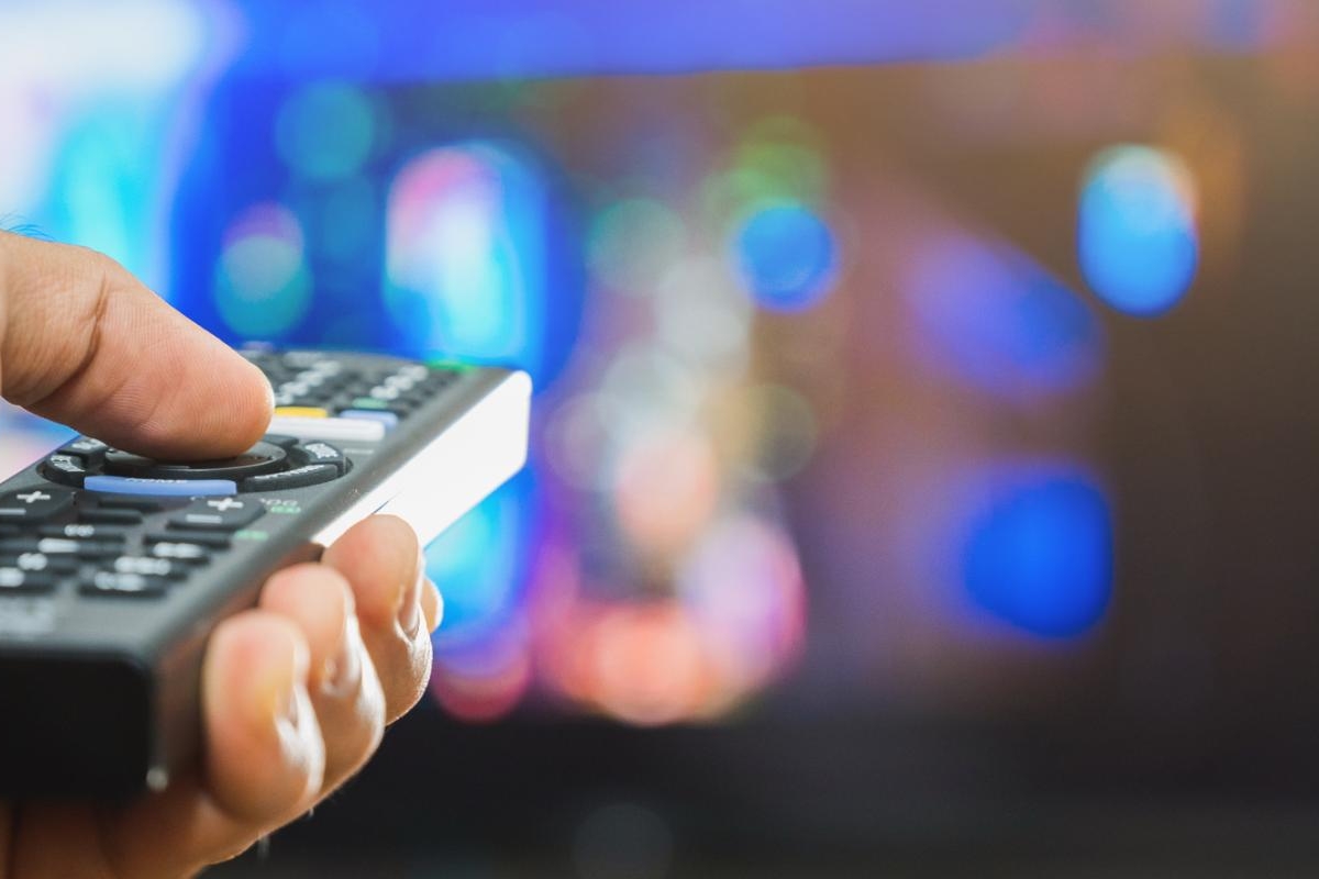 Image of hand holding a TV remote pointed at a colorful screen.