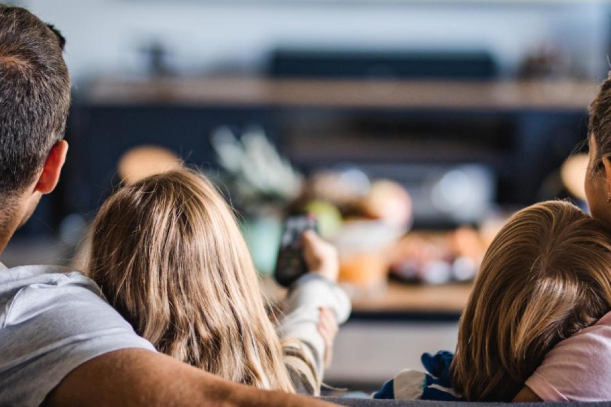 Image of a family sitting together on a couch watching TV.