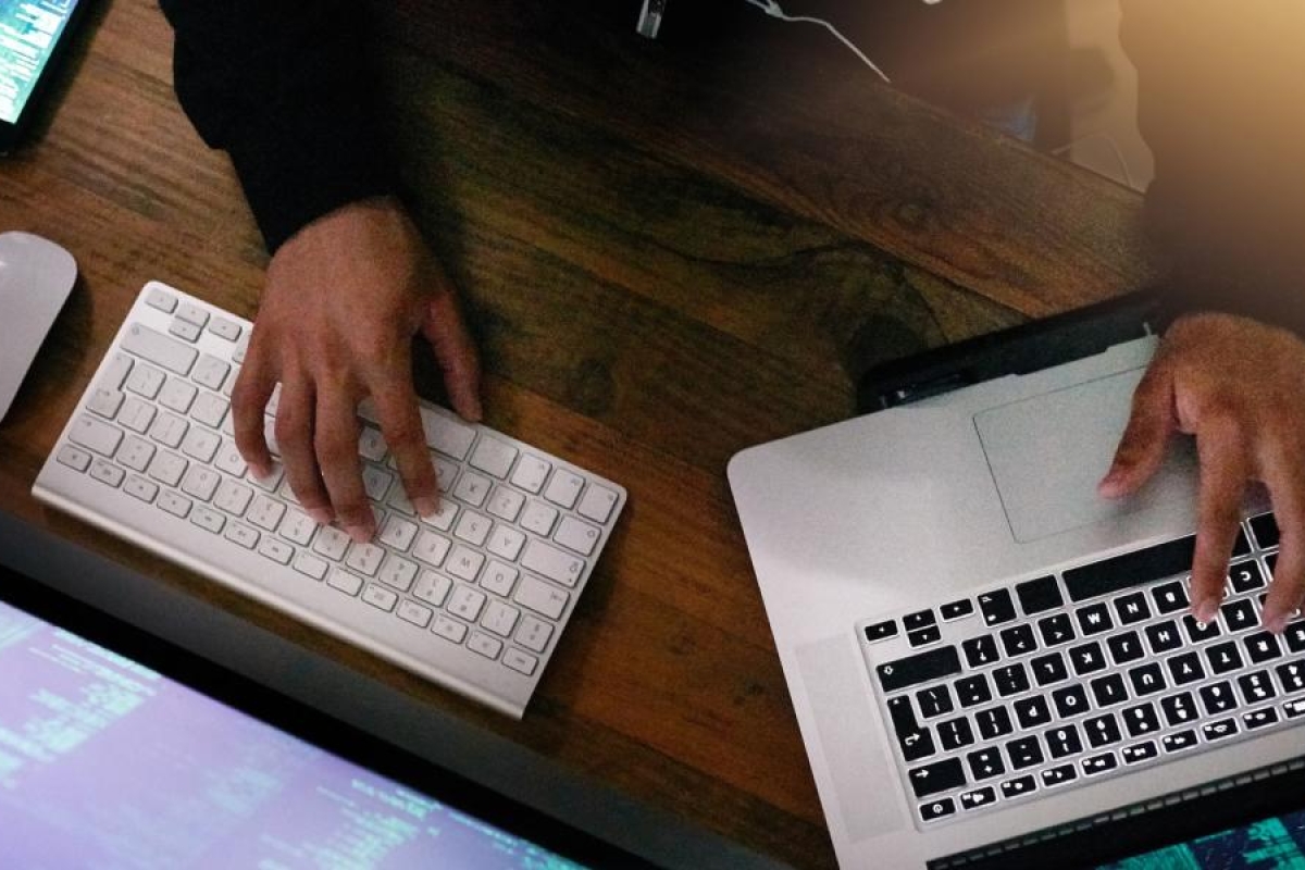 Image of close-up a person working with a laptop, keyboard and monitor.
