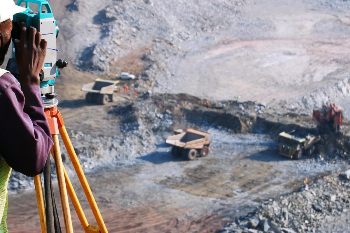 Image of a surveyor using measurement equipment overlooking an open‑pit mining site.