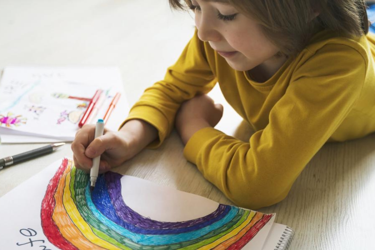 Image of a kid drawing a colourful rainbow.