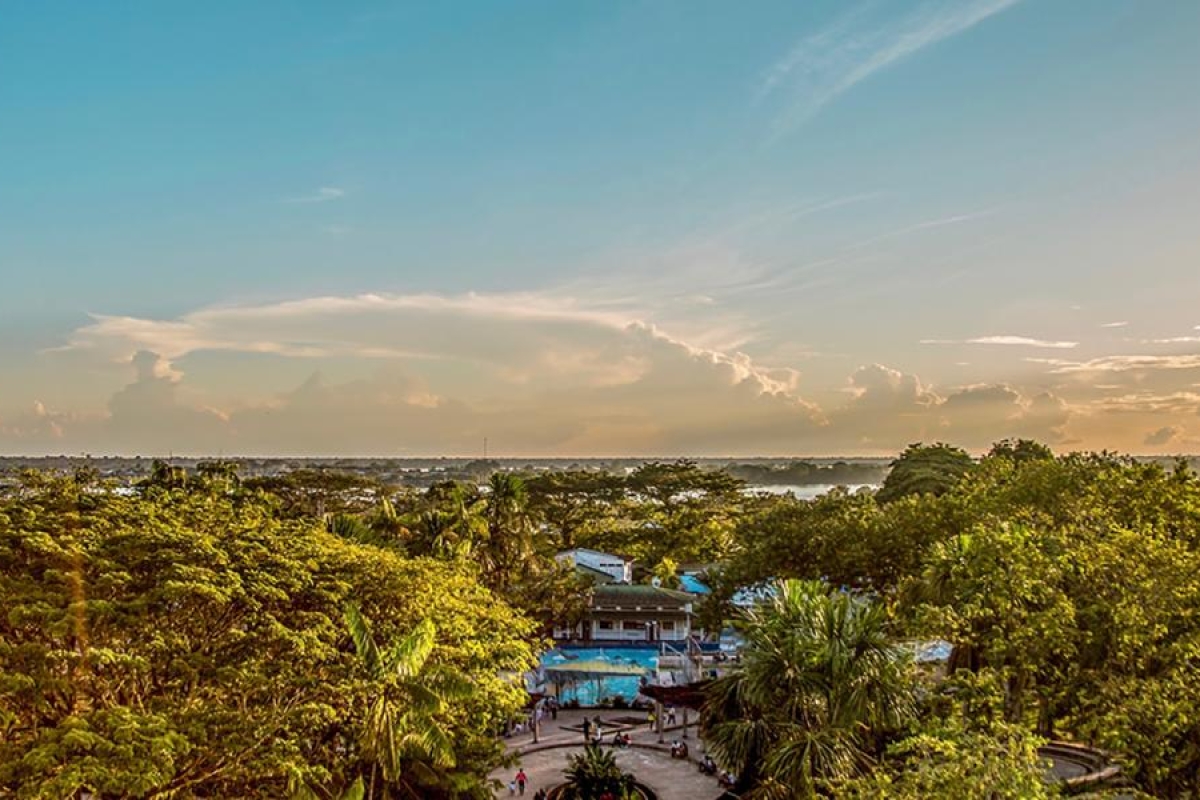 Image of a tropical town surrounded by lush green trees under a warm sunset sky.