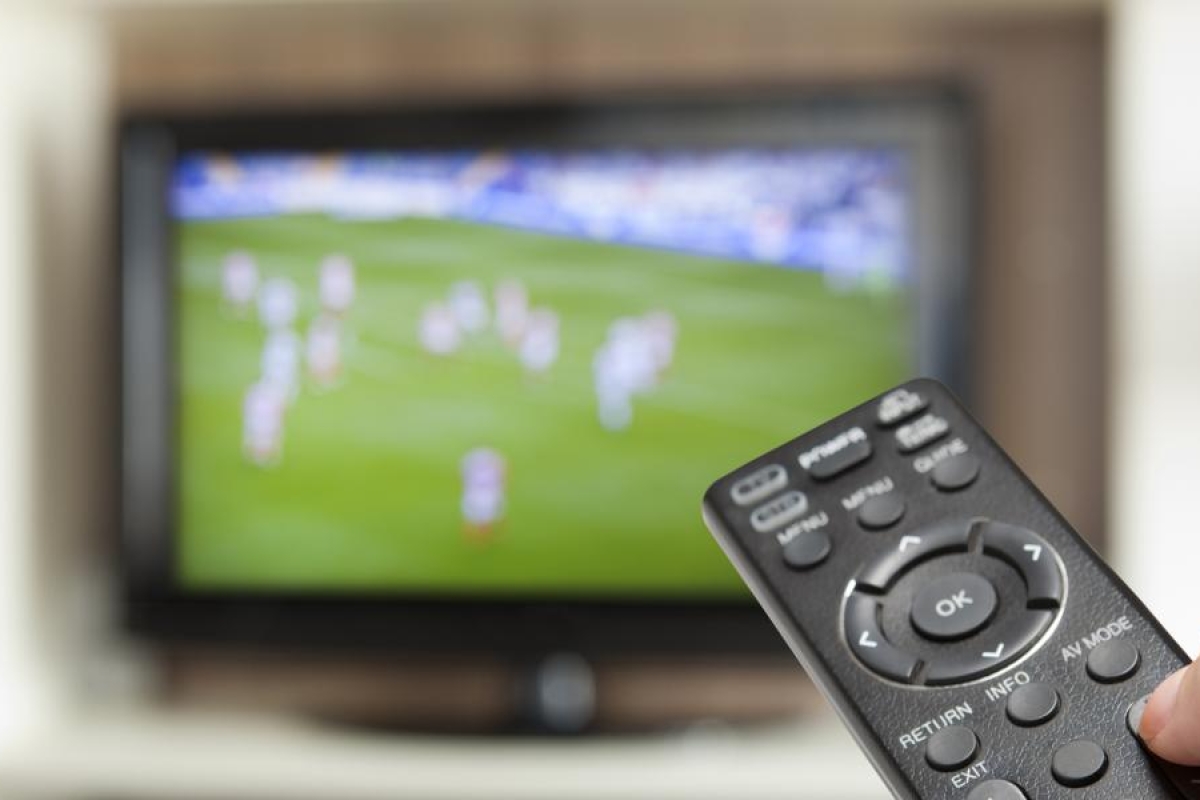 Image of a person's hand holding a remote towards a television.