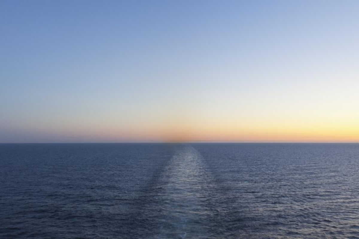Image of open ocean horizon at sunset with a faint wake trail.