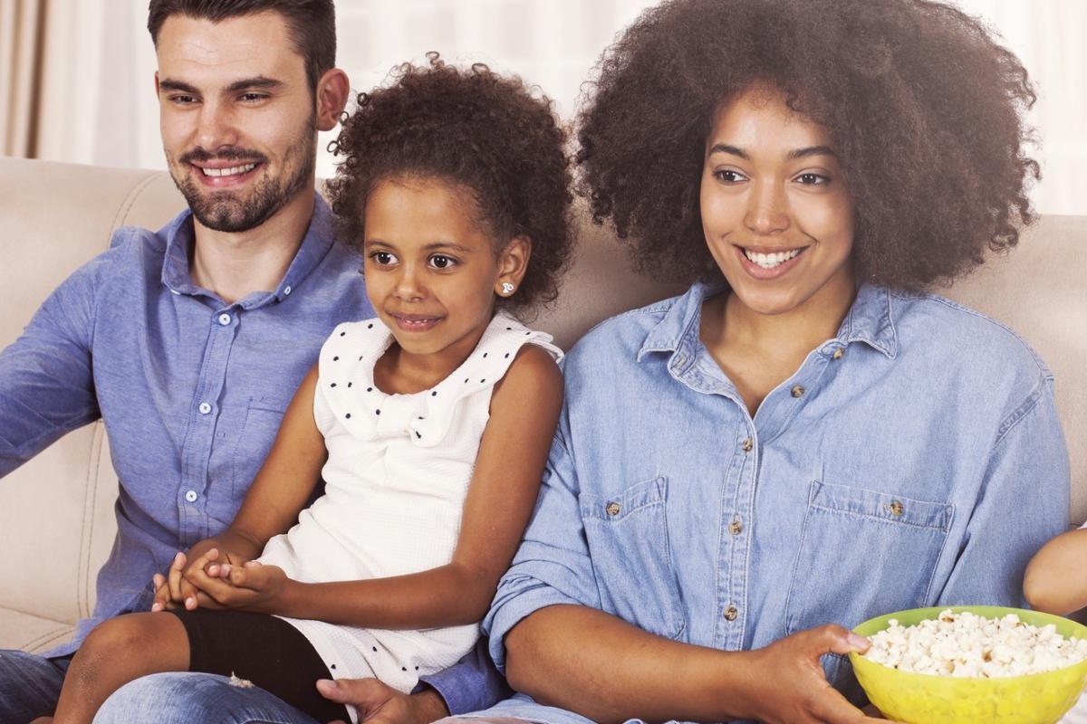 Image of a family sitting on the couch, eating popcorn and watching television.