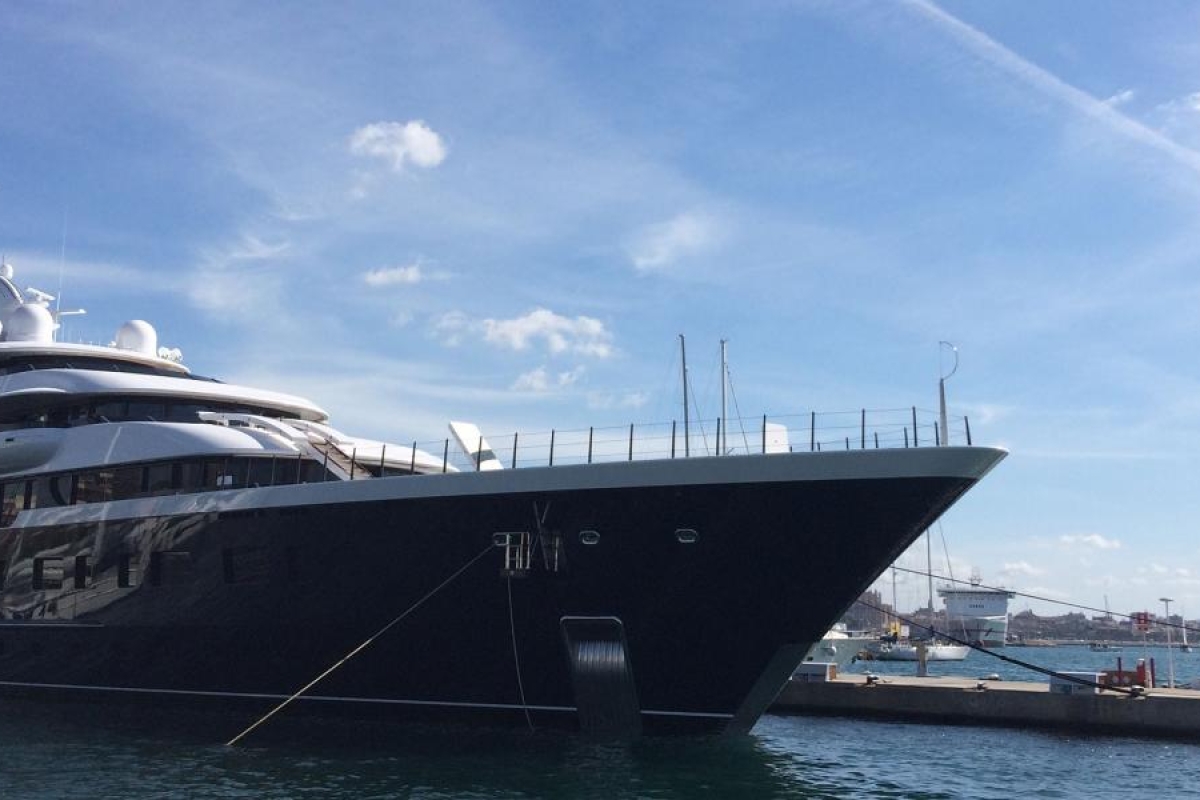 Image of a large luxury yacht docked at a marina under a clear sky.