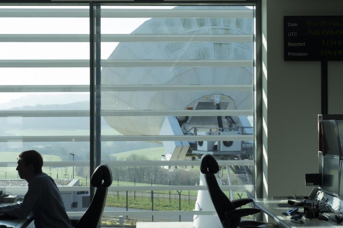 Image of control room monitors facing a large satellite dish outside
