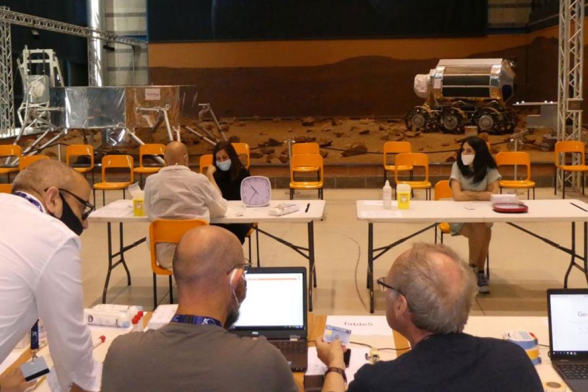 Team working at tables with laptops featuring space‑rover equipment.
