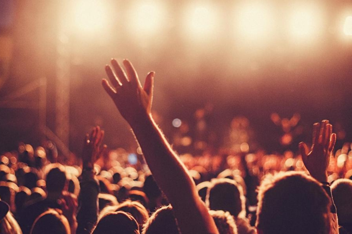 Image of people at a concert raising their hands toward a brightly lit stage.