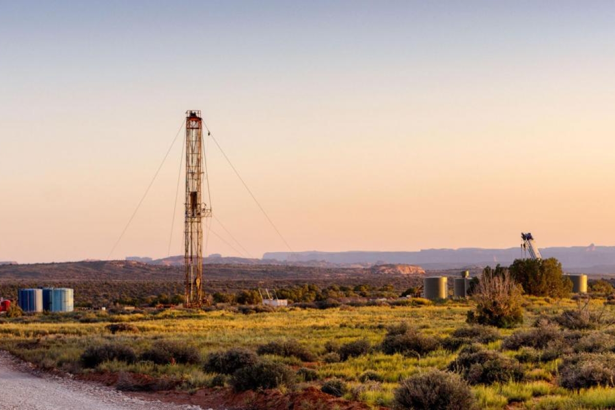 Image of a landscape with a tall drilling rig and storage tanks.
