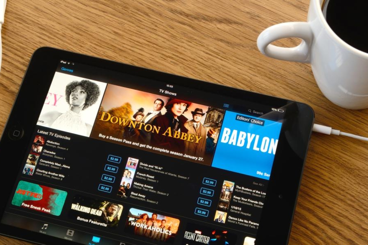 Image of tablet showing TV shows next to earbuds and a cup of coffee.