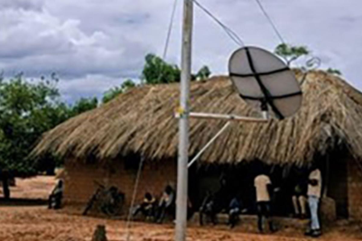A satellite dish beside a thatched-roof building in a rural area.