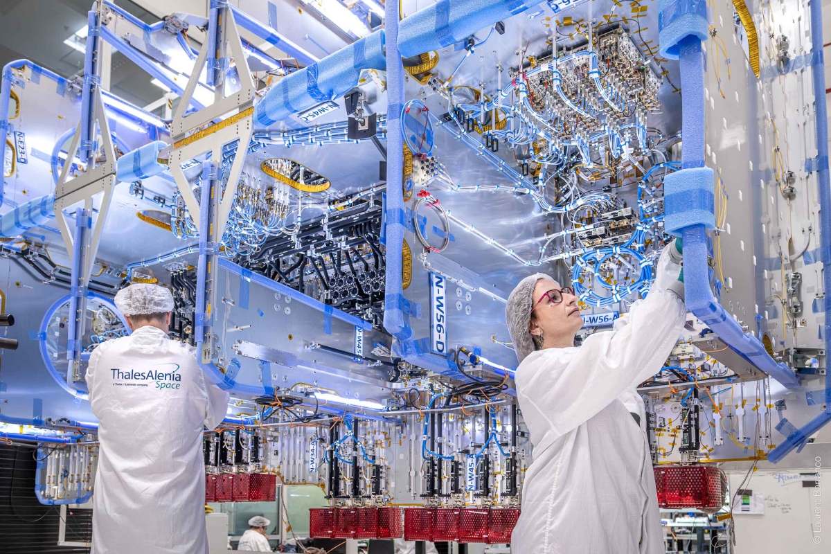 Technicians assembling complex satellite hardware.