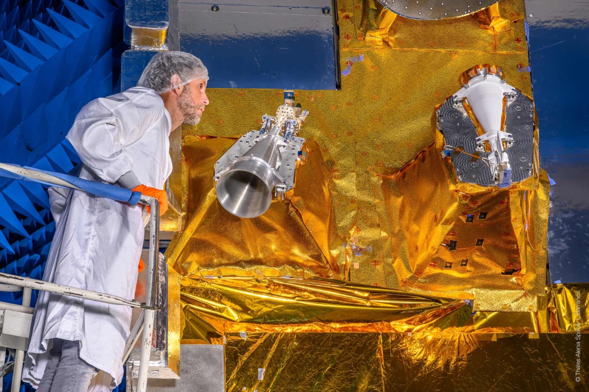 Engineer inspecting satellite components covered in gold thermal foil.