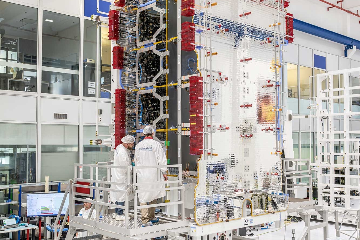 Technicians working on a large satellite module in a cleanroom.