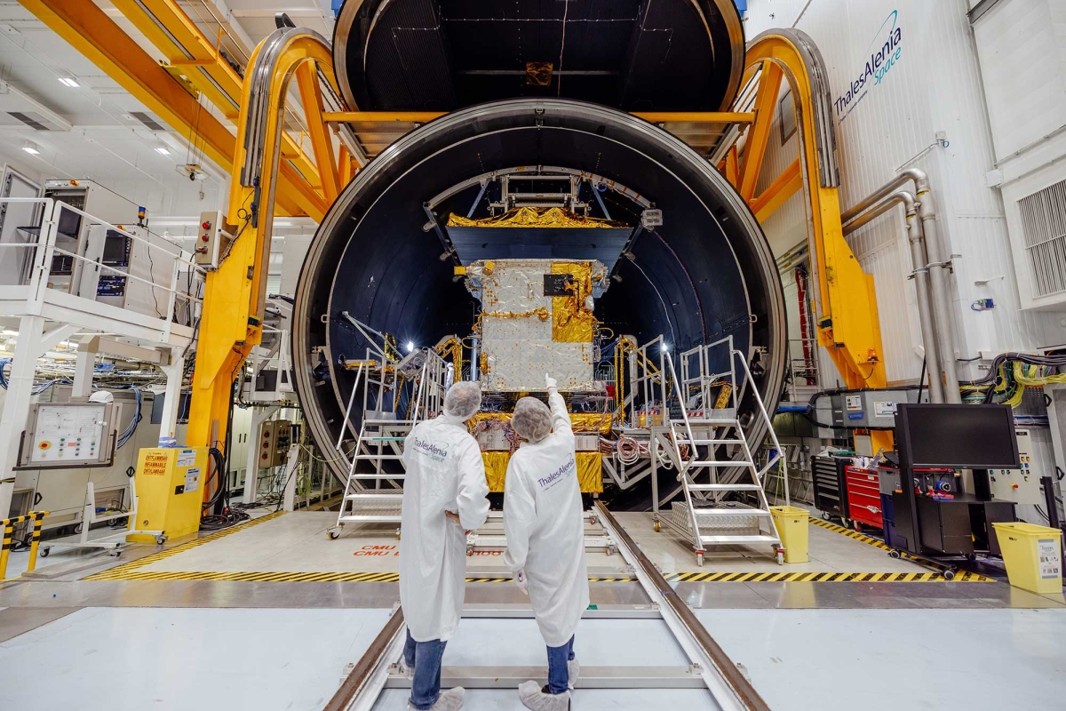 Technicians inspecting a satellite inside a thermal vacuum chamber.
