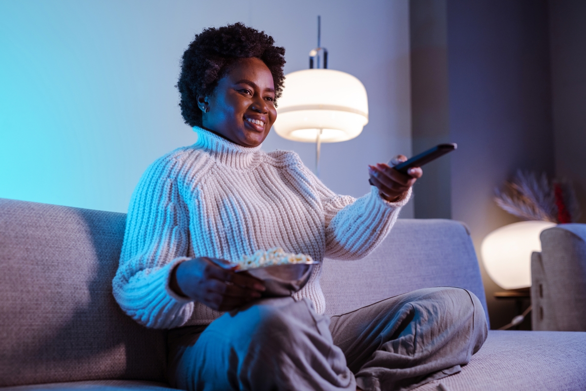 Woman sitting on a couch with popcorn watching television.