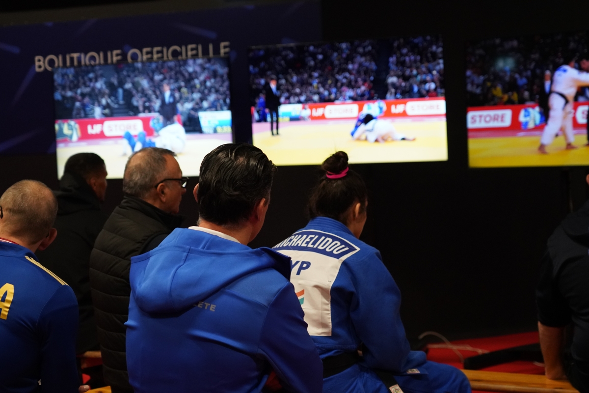 Athletes watching a judo match on multiple screens backstage.