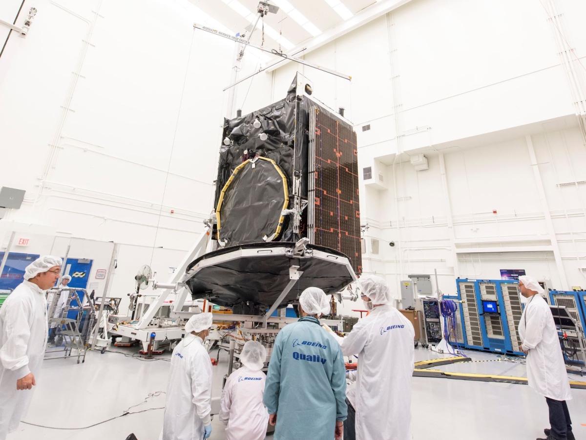 Team of engineers in front of a satellite component in a white room