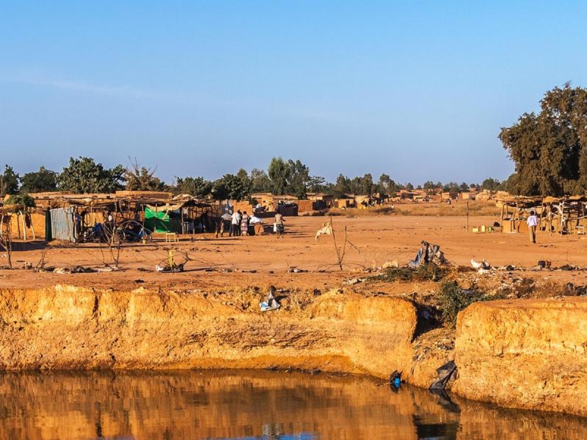 Image of a rural desert village with small clay structures and a water channel in the foreground