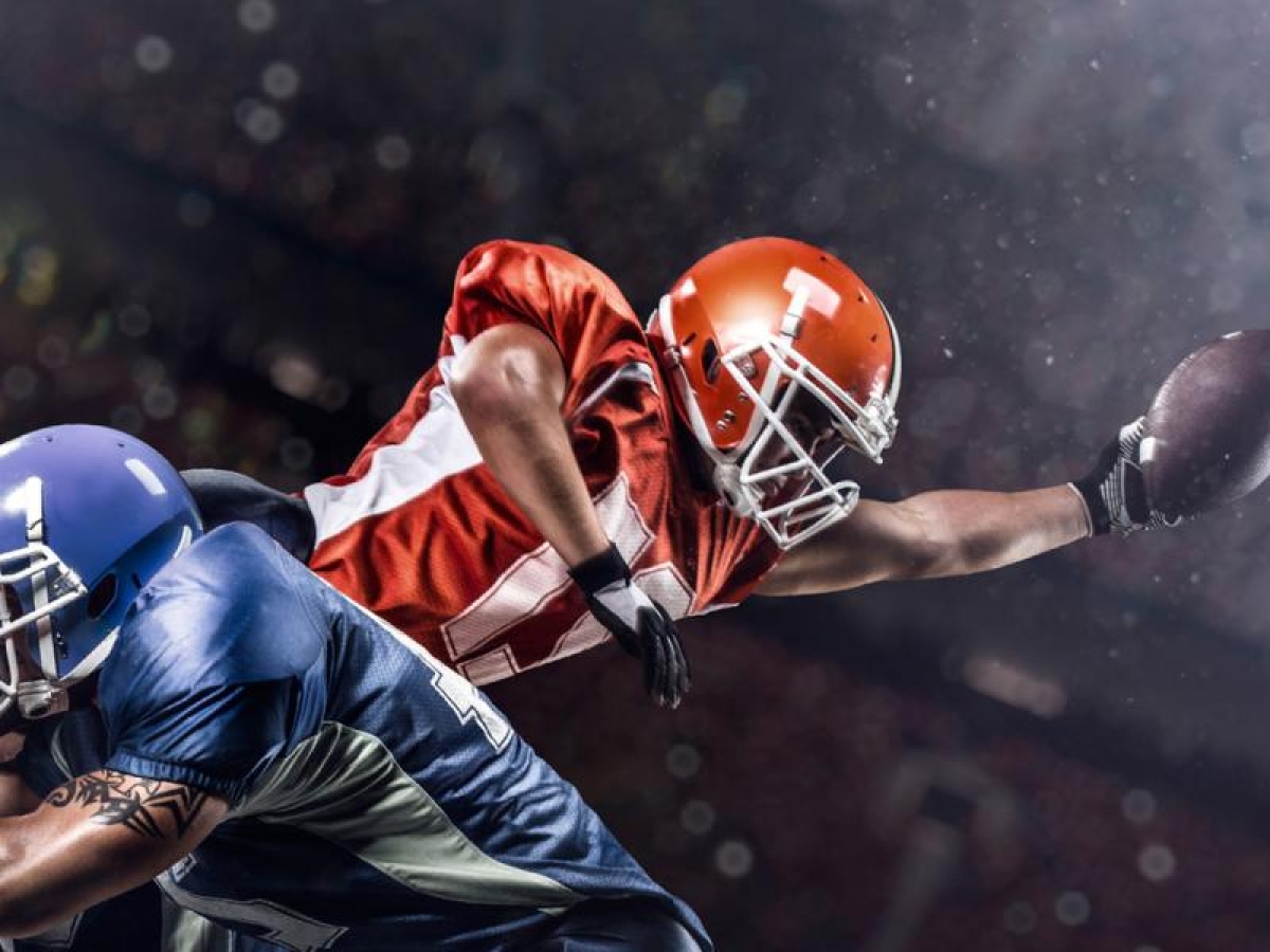 Image of football player diving with the ball while being tackled.