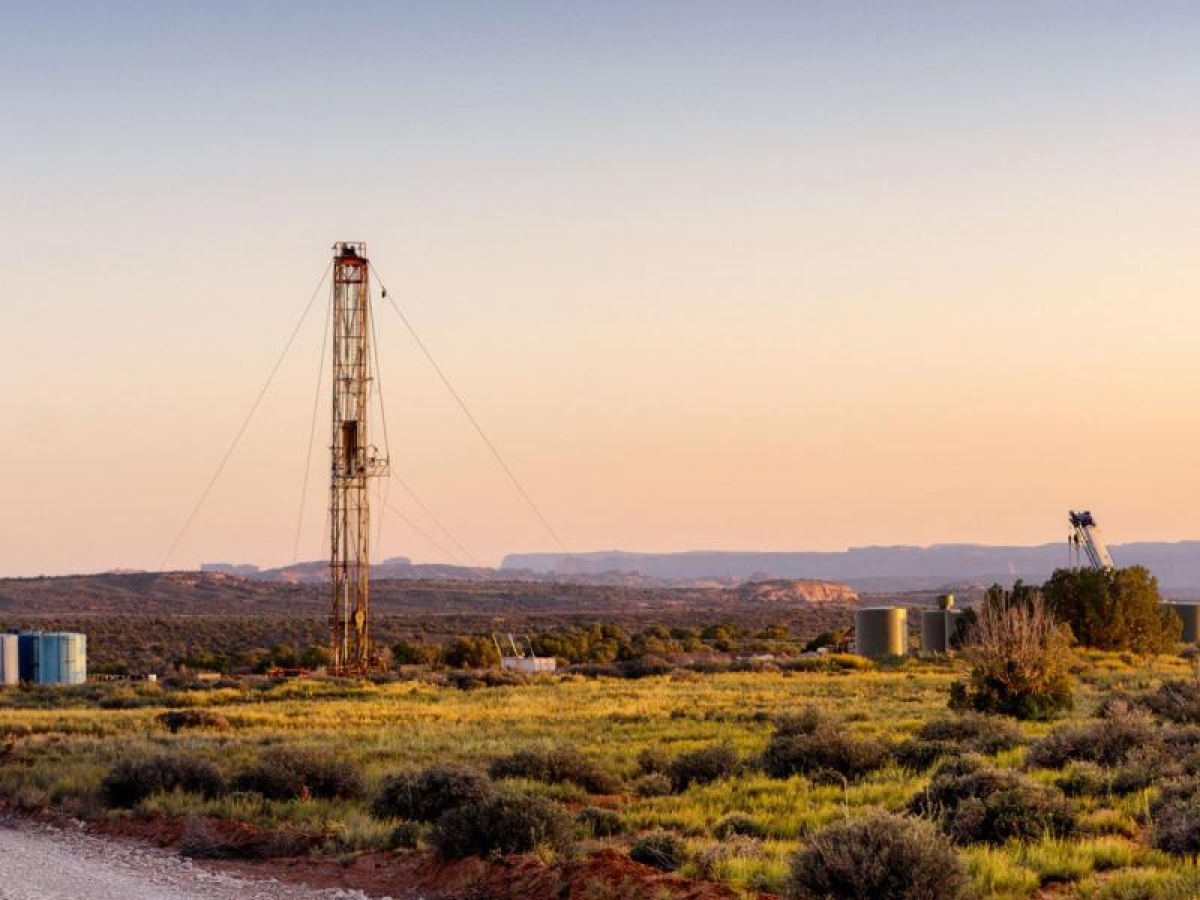Image of a landscape with a tall drilling rig and storage tanks.