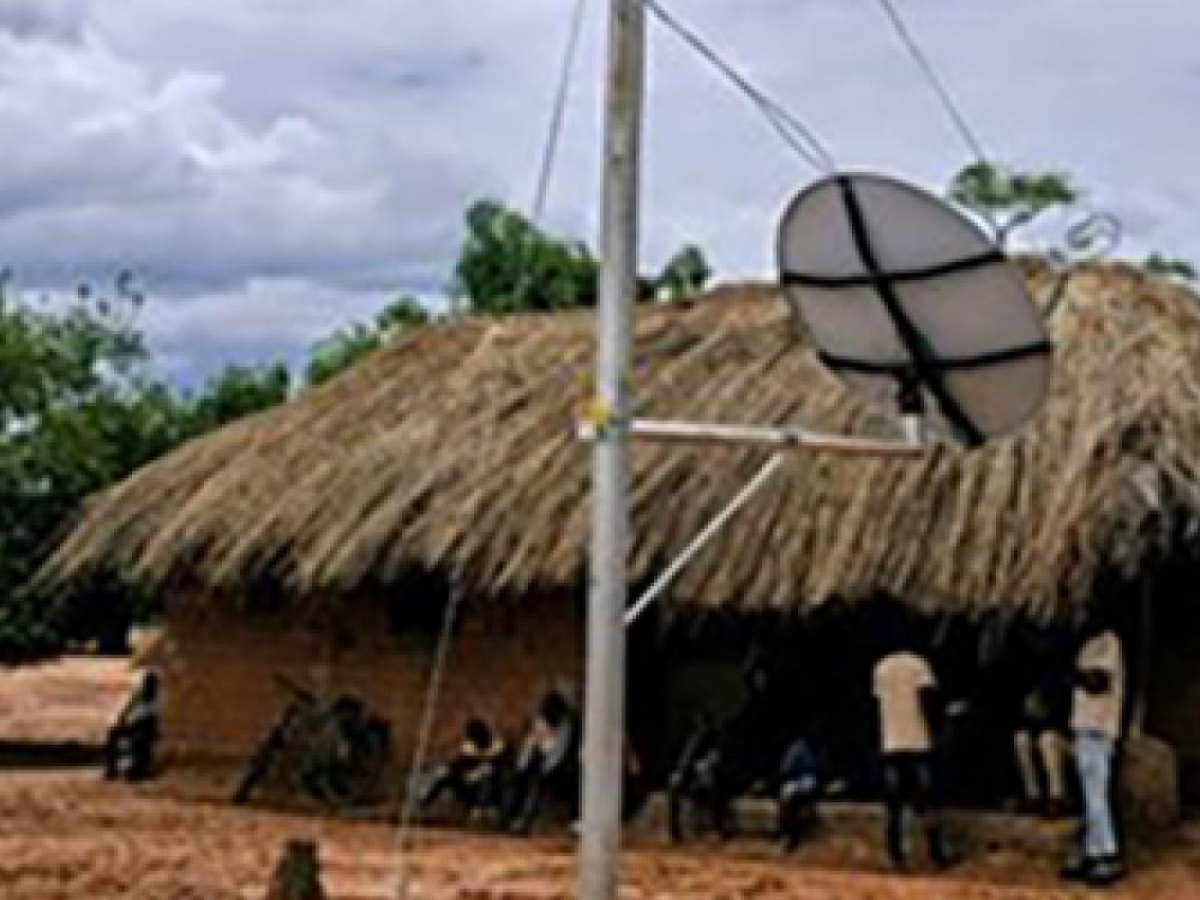 A satellite dish beside a thatched-roof building in a rural area.