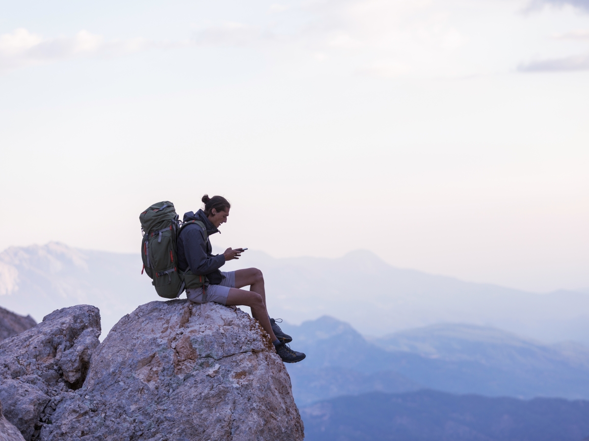 Hiker sitting on a mountain peak using a phone.