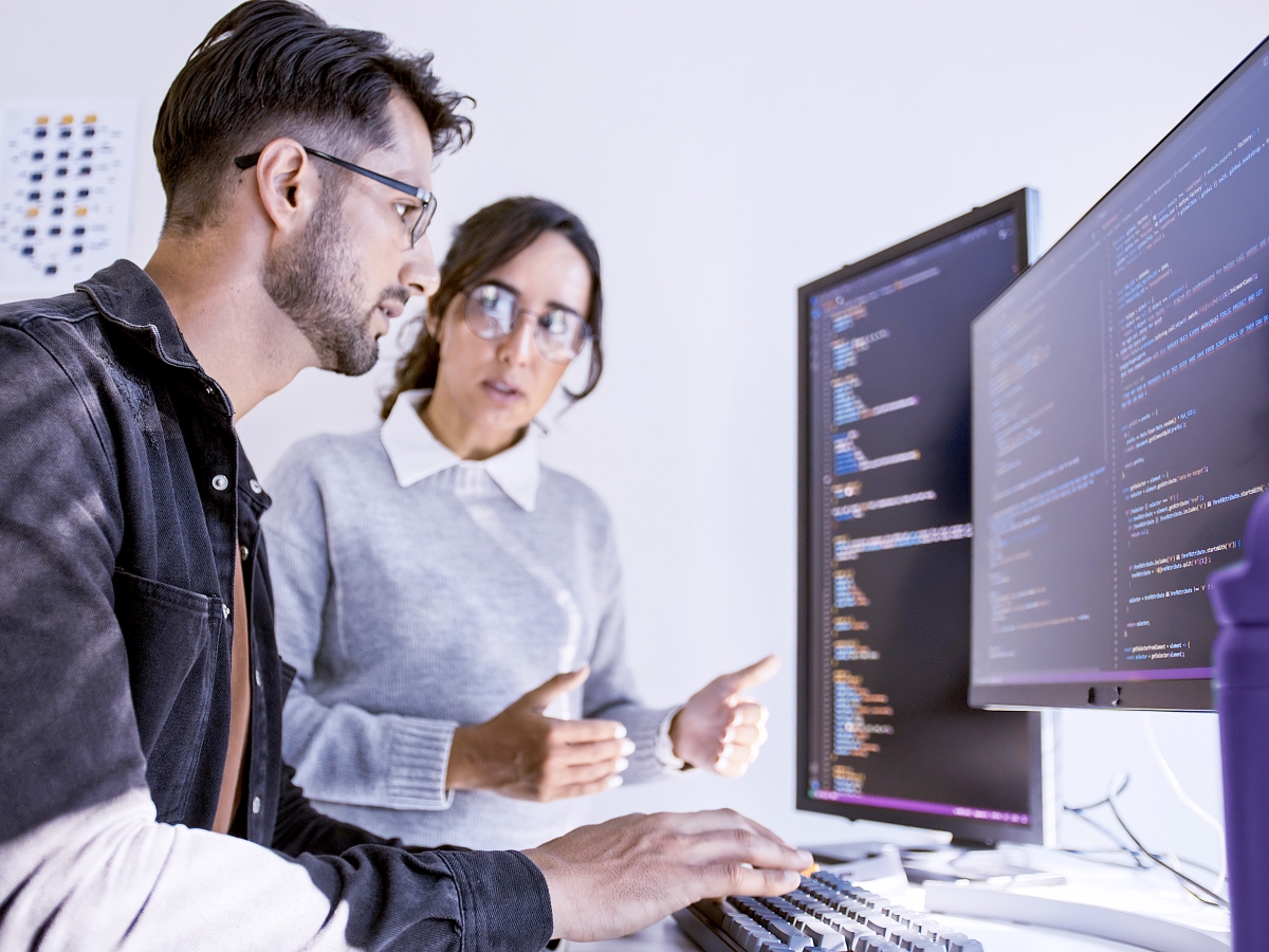 Two people working at a computer with code on the screens.